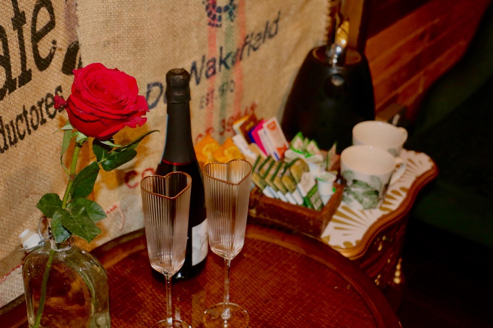 Champagne, heart glasses, rose and tea tray on round table